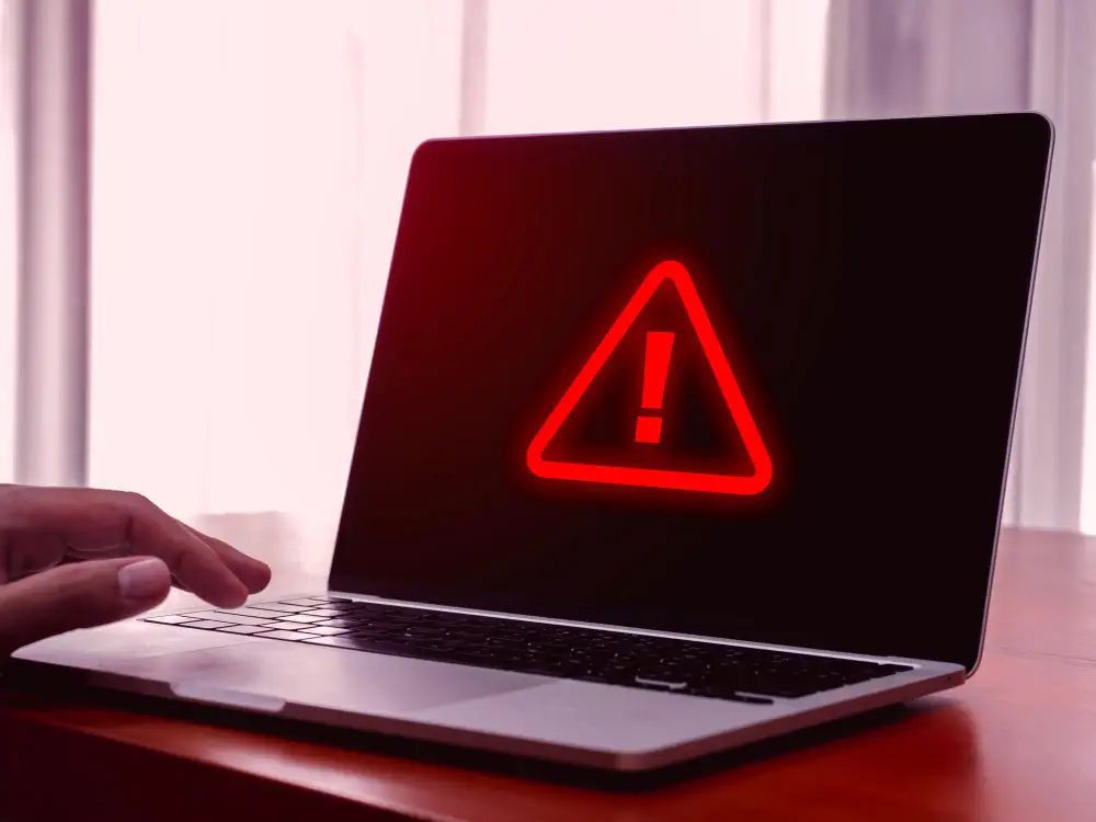 Laptop with red warning icon on screen signaling network connectivity problems or cybersecurity alert.